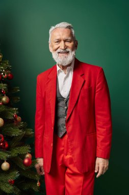 Noel Baba kırmızı kostümlü neşeli adam köknar ağacının yanında süslerle poz veriyor, Noel konsepti.