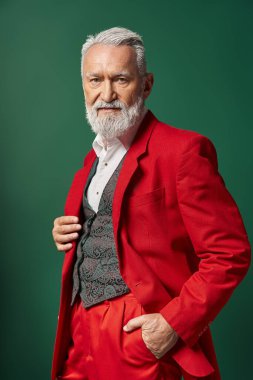 portrait of stylish Santa in elegant red suit posing with one hand in pocket, winter concept clipart