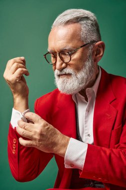 portrait of elegant Santa with beard and glasses fastening button on his sleeve, winter concept clipart