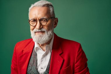 jolly Santa Claus with beard and glasses posing on green backdrop looking at camera, winter concept clipart