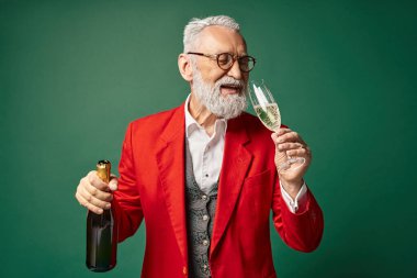 classy jolly Santa Claus enjoying champagne and smiling on dark green backdrop, winter concept clipart