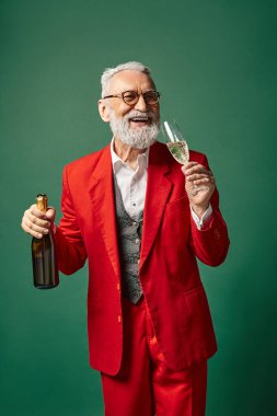 elegant man in Santa Claus outfit tasting delicious champagne on green backdrop, winter concept clipart