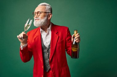 elegant Santa with beard in red classy suit testing champagne on green backdrop, winter concept clipart