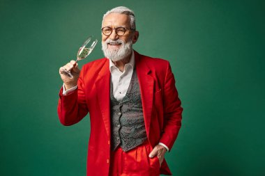 Noel Baba gibi giyinmiş neşeli adam bir eli cebinde şampanya kadehinin keyfini çıkarıyor, kış konsepti.