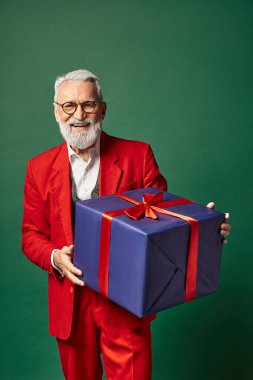 Şık kırmızı elbiseli neşeli Noel Baba elinde kocaman bir hediye ve kameraya gülümsüyor, kış konsepti.