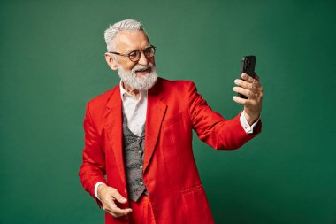 Zarif görünümlü kırmızı elbiseli Noel Baba yeşil arka planda selfie çekiyor, kış konsepti.