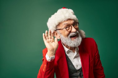 cheerful man dressed as Santa with red hat with hand near ear looking at camera, winter concept clipart