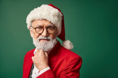 Gözlüklü, sakallı, eli çenesinin altında kameraya bakan zarif Noel Baba, kış konsepti.