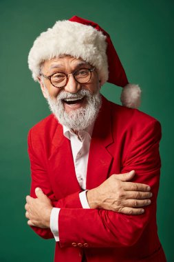 Noel Baba kılığında neşeli bir adam yeşil arka planda poz veriyor ve kameraya gülümsüyor, kış konsepti.