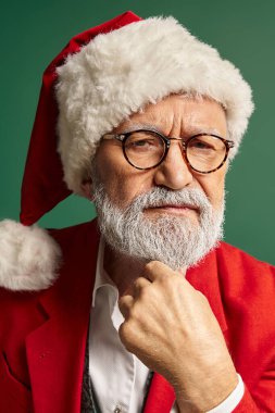 Noel Baba 'nın Noel şapkalı, gözlüklü ve kameraya bakarken çekilmiş dikey bir resmi.