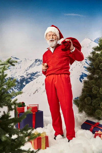 stock image happy Santa with gift bag gesturing surrounded by presents with open mouth, winter concept