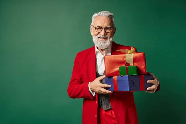 stock image cheerful Santa with glasses posing with pile of presents and smiling at camera, Christmas concept