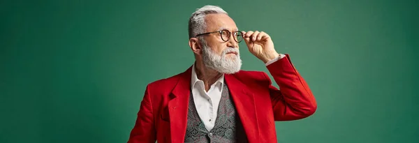 stock image handsome Santa touching his glasses and looking away on green backdrop, winter concept, banner