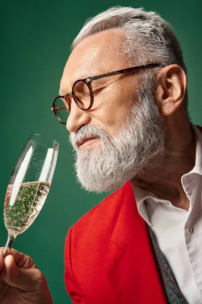portrait of Santa with white beard and glasses enjoying champagne on green backdrop, winter concept