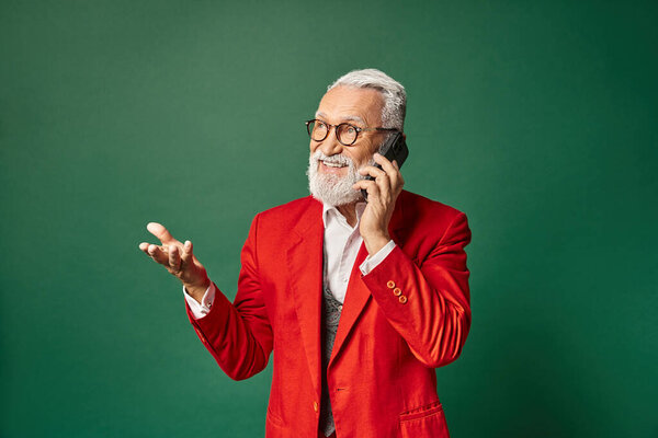 красивый Санта в стильной красной одежде жестикулируя и разговаривая по телефону весело, зимняя концепция