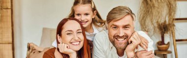 joyful parents with carefree daughter relaxing in bedroom and looking at camera, horizontal banner clipart