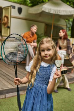Badminton roketleri ve mekik horozu gösteren kız aile ve karavanın yanında bulanık arka planda.