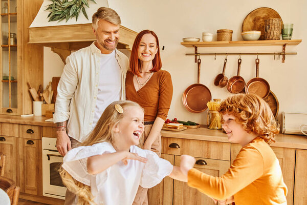 счастливые родители смотрят на беззаботных детей играть и весело провести время на кухне, братья и сестры отношения