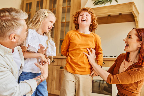 happy parents tickling overjoyed kids in modern kitchen, fun and laughter in cozy home environment