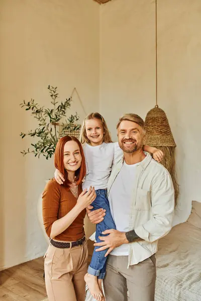 stock image cheerful husband and wife holding cute daughter and looking at camera in cozy bedroom, love and care