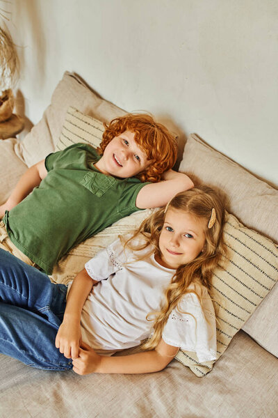 cheerful brother and sister lying on comfortable bed and looking at camera, siblings relationship