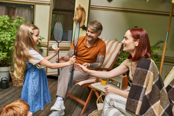 stock image happy girl giving badminton rockets and shuttlecock to parents sitting at modern trailer home