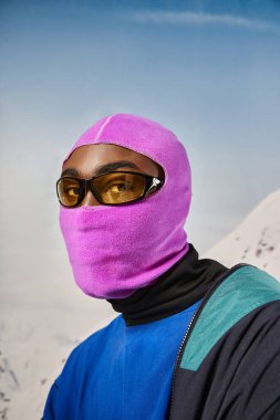 Pembe kar maskeli ve güneş gözlüklü genç Afro-Amerikan adam kameraya bakıyor, kış konsepti
