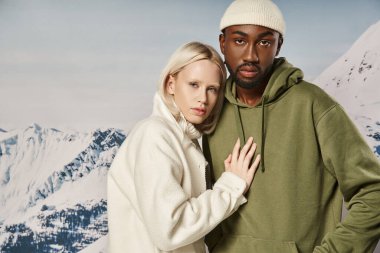 Çekici bir kadın, erkek arkadaşının göğsünde poz veriyor. Dağ manzaralı, şık bir çift.