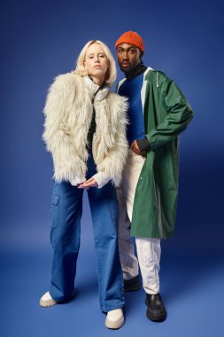 Mavi arka planda kışın şık ırklar arası modeller, sarışın kadın ve Afrikalı Amerikalı erkek.