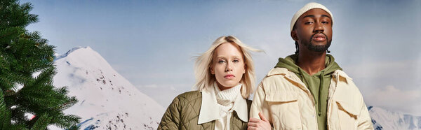 fashionable multiracial couple posing with hand on arm and looking at camera, winter concept, banner