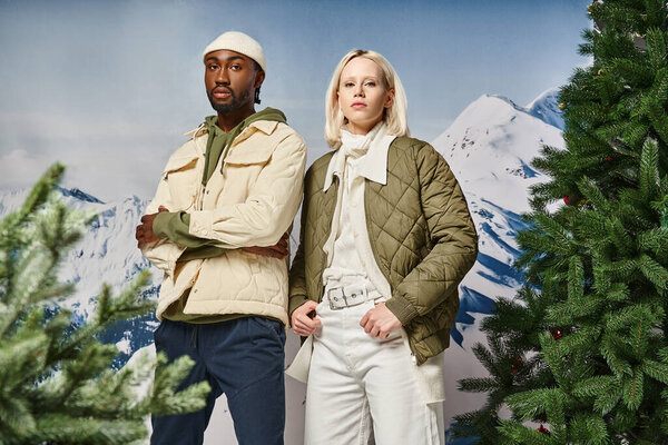 stylish african american with crossed arms posing next to his voguish girlfriend, winter fashion