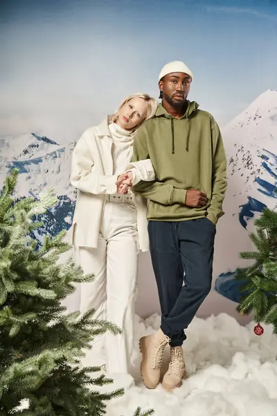 stock image full length of stylish interracial couple in winter attire standing together with mountain backdrop