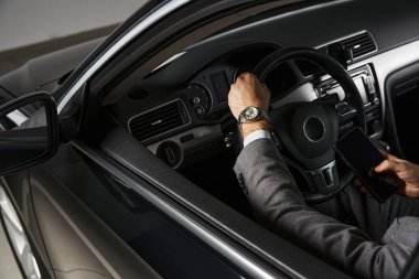 cropped view of elegant professional with wristwatch in stylish suit behind steering wheel, business clipart