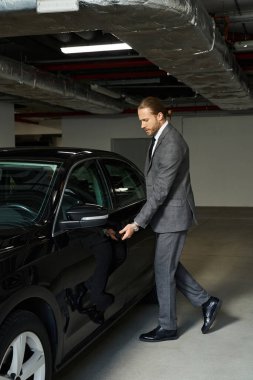 appealing red haired man in smart suit getting into his car on parking lot, business concept clipart