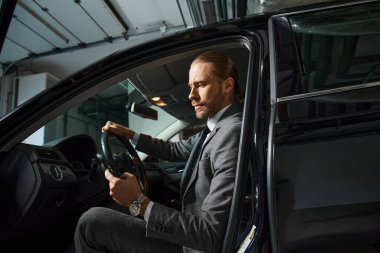 Yakışıklı, sakallı, kırmızı saçlı, şık takım elbiseli, direksiyon başında, iş adamı.