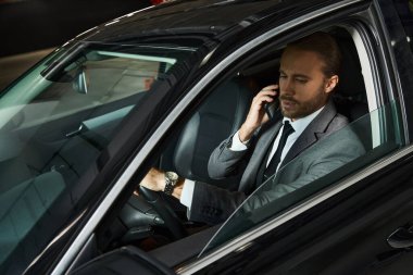 Zarif takım elbiseli çekici sakallı adam direksiyon başında telefonla konuşuyor, iş konsepti.