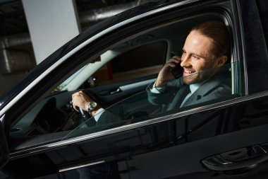 Neşe saçan sakallı yakışıklı adam direksiyon başında telefonla konuşuyor, iş konsepti.