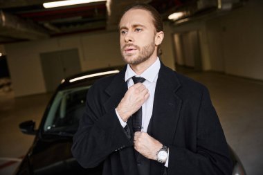 good looking professional in chic smart attire fixing his tie on parking lot, business concept clipart