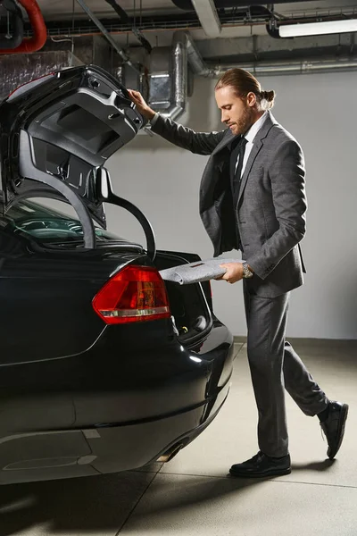 stock image good looking professional in elegant suit with ponytail closing trunk of his car, business concept