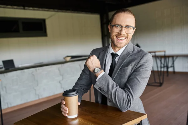cheerful handsome man in gray suit smiling at camera and holding coffee cup, business concept