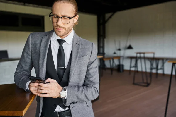 handsome professional in smart gray suit looking attentively at his mobile phone, business concept