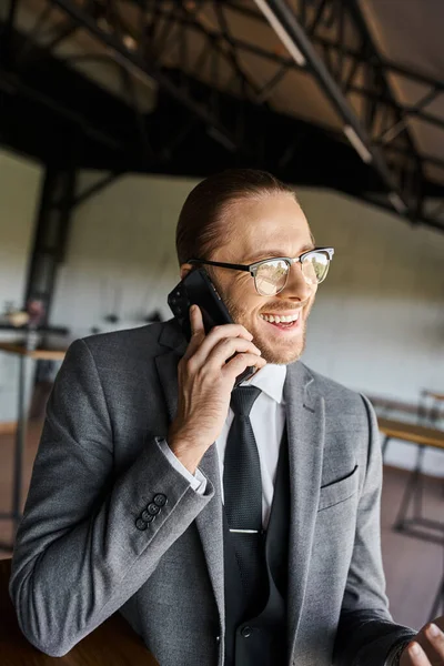 cheerful elegant businessman in chic gray suit talking actively by phone and smiling happily