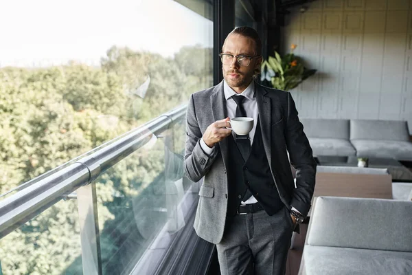 stock image handsome stylish professional with glasses drinking tea and posing next to window, business concept