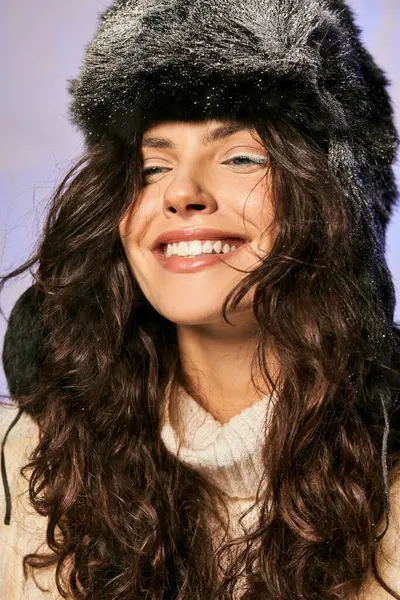 stock image brunette woman with furry hat and white attire looking at camera on grey backdrop, winter fashion