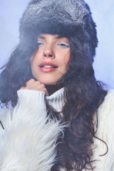 brunette young woman with winter hat and white cozy attire posing on grey backdrop, cool air