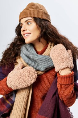 Kış modası, örgü şapkalı neşeli genç kadın ve gri arka planda gülümseyen eldivenler.