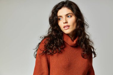 Terracotta örgü süveter giyen güzel esmer kadın gri arka plana bakıyor, kış modası.