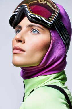 portrait of woman in ski clothes with balaclava looking up on grey, female model with blue eyes clipart