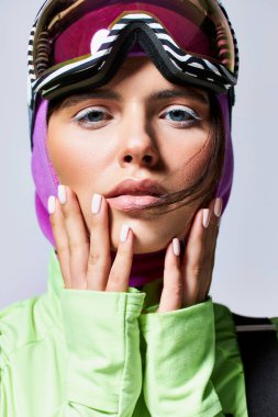 close up of pretty woman in active wear with balaclava on head looking at camera on grey background clipart