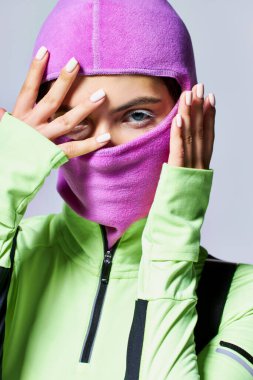 Mor kar maskesi takan mavi gözlü bir kadının portresi ve gri arka planda kameraya bakması.